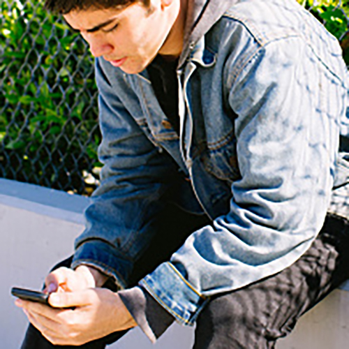 Adolescente masculino sentado en la pared mirando teléfono celular