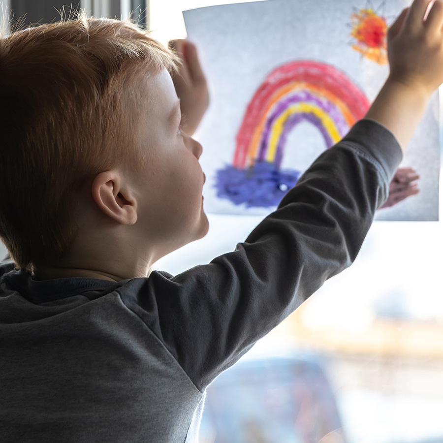 child holding a rainbow drawing up to a window